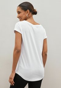 Vit t-shirt med kort ärm och avslappnad passform, rund halsringning och uppvikt ärmdesign, kombinerad med svarta leggings.