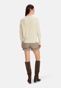 Cremfarbener Pullover, strukturierte braune gemusterte Shorts und knielange braune Stiefel mit Blockabsatz. Das Outfit hat eine lockere Passform und gerippte Details.