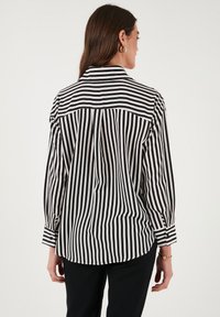 Black and white striped blouse with a collared neck, long sleeves, and cuffed wrists. Fabric appears smooth with a relaxed fit.
