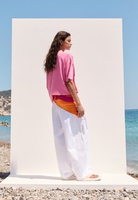 Løst siddende pink t-shirt kombineret med brede hvide bukser. Outfittet har et farverigt orange silkeaccent. Glatte teksturer, minimalistisk design.