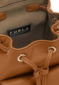 Interno di una borsa a tracolla in pelle marrone con rivestimento in tessuto grigio. Presenta hardware in tonalità oro e un'etichetta del marchio che reca la dicitura "FURLA PELLE VERA."