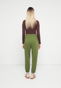 Joggers verde oliva con puños ajustados, cinturilla elástica y textura suave, combinados con una camiseta de manga larga marrón ajustada.