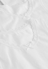 Twee witte katoenen tanktops met een golvende kantafwerking langs de halslijn, met kleine decoratieve strikjes in het midden.