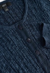 Cardigan bleu marine texturé présentant un design côtelé, un col rond et quatre boutons noirs le long de la patte de boutonnage avant.