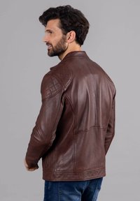 Brown leather jacket with a fitted design, quilted shoulder accents, and a smooth texture. The back features subtle stitching details.
