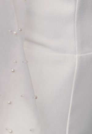 Detail bílého materiálu s průsvitnou vrstvou zdobenou rozptýlenými malými a středními perlovými korálky.