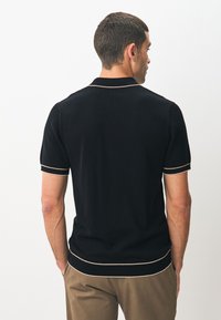 Zwart gebreid poloshirt met korte mouwen, voorzien van een gestructureerd ontwerp, een roomkleurige geribbelde kraag en zoomaccenten.