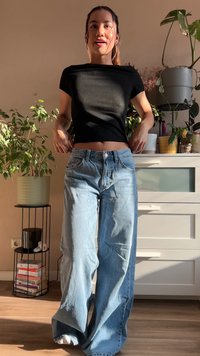Sort tætsiddende top med korte ærmer parret med lyseblå vidde jeans. Blød denimtekstur, synlig søm og en frontknap.