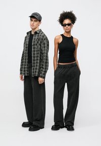 Musta-harmaaruudullinen paita, musta hihaton toppi, löysät harmaat kirjailulla koristellut housut ja massiiviset mustat kengät. Asusteina lippalakki ja aurinkolasit.