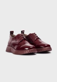 Zapatos de charol burdeos con punta redonda, diseño de cordones y suela de goma estriada. Presentan una tira en el talón para facilitar el calzado.