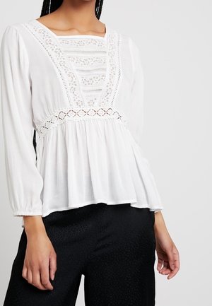 Witte blouse met lange mouwen, inzetstukken van kant, een vierkante halslijn, een getailleerde taille en een losvallende zoom, gecombineerd met zwarte gelede broek.