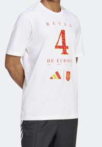 Hvid bomulds t-shirt med "REYES 4 DE EUROPA" i rød og gul, samt Adidas-logo og Spaniens emblem trykt på forsiden. Korte ærmer.