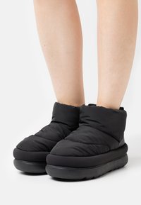 Botas de tobillo acolchadas negras con una textura suave y acolchada y suelas de goma gruesas. Diseño minimalista con puntera redondeada y un ligero dobladillo.