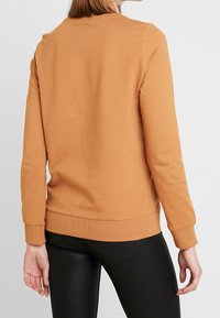 Bruine katoenen sweatshirt met lange mouwen, ribbels bij de manchetten en zoom. Glad textuur, ronde hals ontwerp, minimalistische stijl.