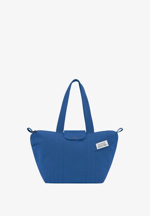 Blue canvas tote bag with two long handles, a button closure, and a side pocket featuring a label, structured and spacious design.