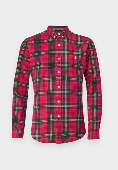 Κόκκινο καρό πουκάμισο με ντεκολτέ που κουμπώνει, μακριά μανίκια και λευκά κουμπιά. Έχει πράσινες και κίτρινες λεπτομέρειες στο σχέδιο.