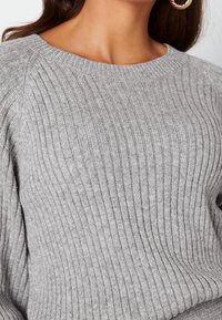Pull en tricot gris avec une texture côtelée, présentant un col large et des manches longues. Le fil présente une légère variation de couleur.