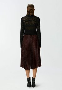 Un pull en tricot noir avec un dos texturé, associé à une jupe plissée bordeaux à pois blancs et des bottines noires brillantes.