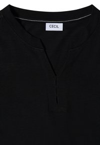 Encolure de chemise noire avec une petite fente en V et trois détails de couture horizontaux sous le col avec une étiquette blanche portant la mention "CECIL".