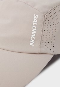 Light beige running cap made of soft fabric, features perforations for ventilation, with "SALOMON" logo in white on the side.