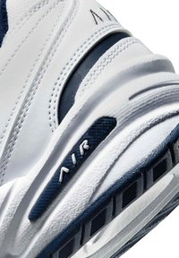 Sneaker med överdel i vitt läder med marinblå detaljer, texturerade sidor och synlig "AIR"-logotyp på mellansulan.