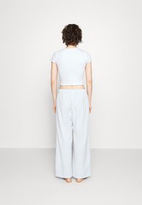 Ljusgrå kort t-shirt med volangkanter, ihop med löst sittande, randiga pyjamasbyxor. Outfiten har en avslappnad passform och mjuk textur.