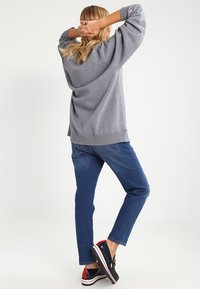 Harmaa huppari, jossa on tippuneet olkapäät, yhdistettynä sinisiin farkkuihin ja tummiin kenkiin, joissa on punaisia, valkoisia ja laivastonsinisiä yksityiskohtia. Rentoa istuvuutta, pehmeä kangas.