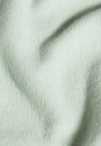 Jasnozielona dzianina o miękkiej teksturze, z delikatnym wzorem szydełkowym i subtelnymi wariacjami na powierzchni.