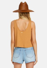 Hnedý rebrovaný crop top s nízkym chrbtom a zlatou nášivkou, skombinovaný so svetlomodrými zničenými džínsovými šortkami so strapcami.