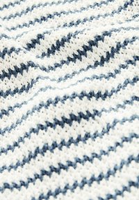 Gros plan sur un tissu tricoté doux avec des rayures diagonales alternées épaisses et fines de couleur bleu marine et blanc.