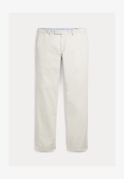 Pánske nohavice v úzkom strihu v krémovo bielej farbe, s pútkami na opasok, bočnými vreckami a skrytým predným zipsom na neutrálnom pozadí.