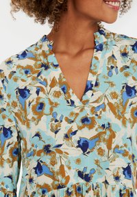 Rochie cu imprimeu floral, pe un fundal albastru deschis, cu flori albastre și maronii. Design cu decolteu în V, cu bandă volan și textură netedă.