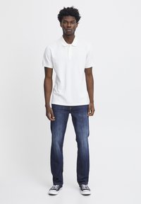Vit pikétröja med krage, parsad med blå denimjeans med rak passform och subtila blekningar, kompletterad med svarta sneakers.