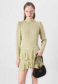 Rochie galbenă cu un model, guler înalt și hem peplum, asortată cu o geantă de mână neagră, tip quilted, cu accesorii aurii și un mâner curbat.