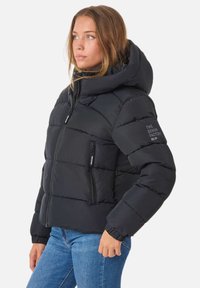 Svart pufferjacka med huva, med dragkedja fram, två sidofickor och elastiska muddarna. Textdetalj på ärmen.