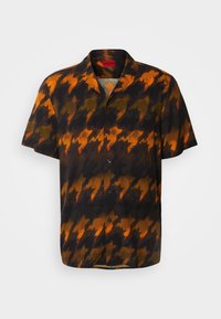 Chemise à manches courtes avec grand motif pied-de-poule en noir, orange et tons brun foncé, col et poche avant visibles.