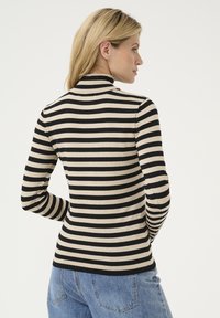 Beige värvi pikakäised turtleneck-särk mustade horisontaalsete triipudega, millel on figuuri rõhutav lõige ja soonikkoes kaelus. Seljas sinised teksapüksid.