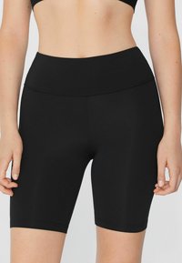 Pantalones cortos deportivos negros hechos de una tela suave y elástica, con una cintura alta y longitud hasta la mitad del muslo, presentando un detalle de costura mínimo.