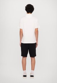 Tricou alb pentru bărbați, cu mânecă scurtă și decolteu rotund, combinat cu pantaloni scurți negri, având o croială lejeră și un design minimalist. Pantofi cu talpă din cauciuc.