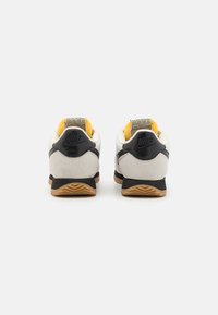 Ett par vita, svarta och beige Nike-sneakers sedd bakifrån mot en vit bakgrund.