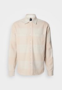 Chemise beige à manches longues avec boutons, deux poches poitrine et col classique, présentée sur fond blanc uni.
