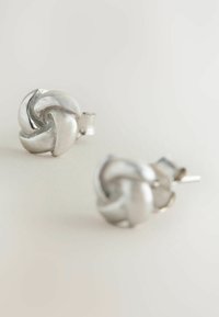 Pair of silver stud earrings with a twisted knot design on a light neutral background.