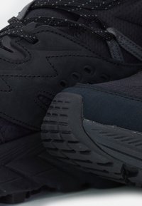 Scarpe sportive nere caratterizzate da una combinazione di materiali testurizzati, una suola con motivo e lacci scuri con sottili accenti riflettenti.