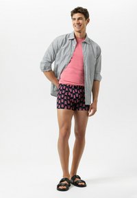 Gestreiftes Hemd mit Knöpfen, pinkes T-Shirt, gemusterte marineblaue Badeshorts mit pinken Akzenten und schwarze Slide-Sandalen.