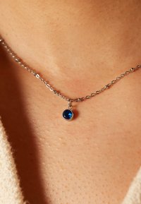Zilveren ketting met een ronde, blauwe edelsteen hanger. De ketting is delicaat met ovale schakels en ligt op de huid.