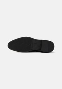Semelle de chaussure noire avec une finition lisse, présentant un motif de semelle texturé pour une adhérence et une durabilité accrues. Forme frontale arrondie avec un branding subtil.