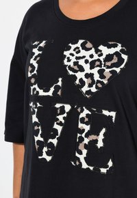 Sweat à tissu noir avec un cœur en imprimé léopard à l'intérieur du mot "LOVE", avec un col rond et des manches trois-quarts.