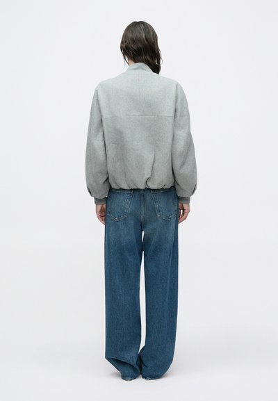 Veste grise surdimensionnée avec un col montant, un ourlet côtelé et un jean bleu en denim ample assorti, avec une texture délavée et des poches arrière proéminentes.