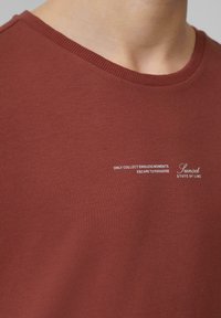 Rode katoenen T-shirt met een ronde hals, met witte tekst "ENKEL EINDLOZE MOMENTEN VERZAMELEN" en "Zonsondergang TOESTAND VAN DE LIJN."
