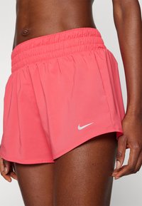 Pantalones cortos deportivos rosa con una cinturilla elástica, hechos de tela ligera. Presenta un pequeño logotipo de Nike en blanco en el dobladillo inferior.
